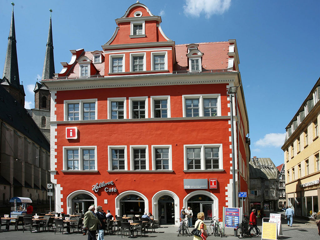 Historisches Marktschlösschen mit roter Fassade vor blauem Himmel, im Hintergrund die Marktkirche