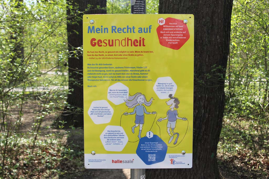Station 7 - Spielplatz Würfelwiese. Tafel zum Thema Recht auf Gesundheit. im Hintergrund sind Bäume zu sehen