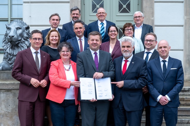 Bei der Unterzeichnung waren der Ministerpräsident Sachsen-Anhalts Sven Schulze sowie die Landesminister Prof. Armin Willingmann (Wissenschaft), Michael Richter (Finanzen), Petra Grimm-Benne (Gesundheit) und Oberbürgermeister Dr. Alexander Vogt anwesend.  Hier stehen alle bei der Unterzeichnung Anwesenden vor dem Löwengebäude als Gruppenbild
