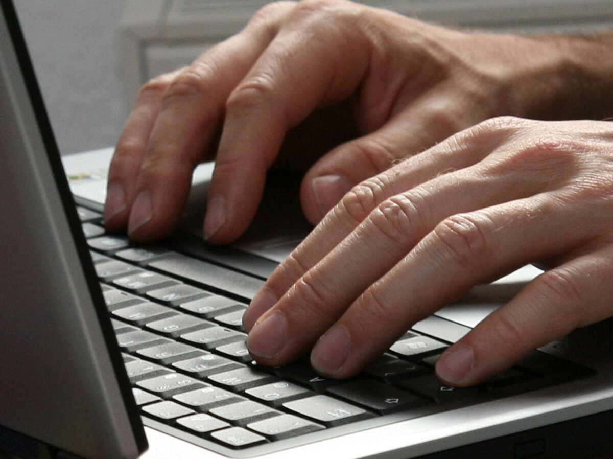 Hände geben auf einer Tastatur eines Laptops etwas ein