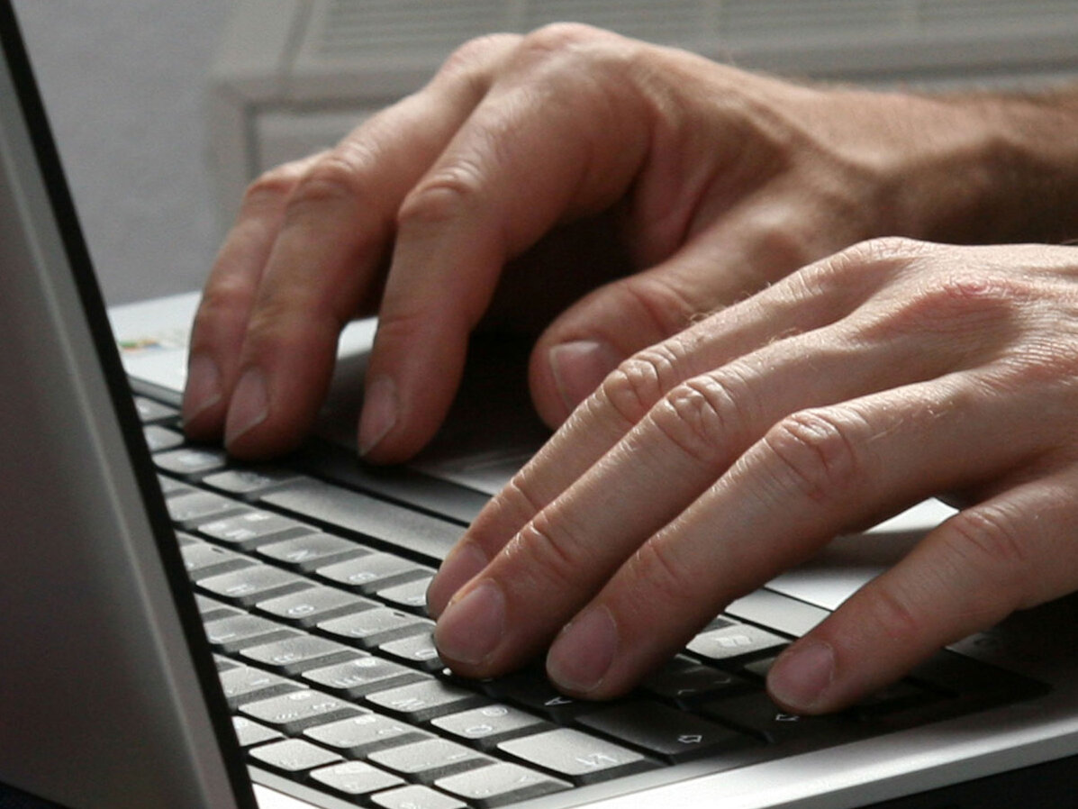 Hände geben auf einer Tastatur eines Laptops etwas ein