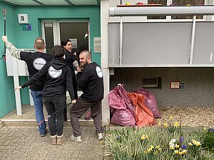 4 Mitarbeitende vom Projekt stehen vor Hauseingang. Rechts daneben stehen befüllte Müllsäcke unter dem Balkon.