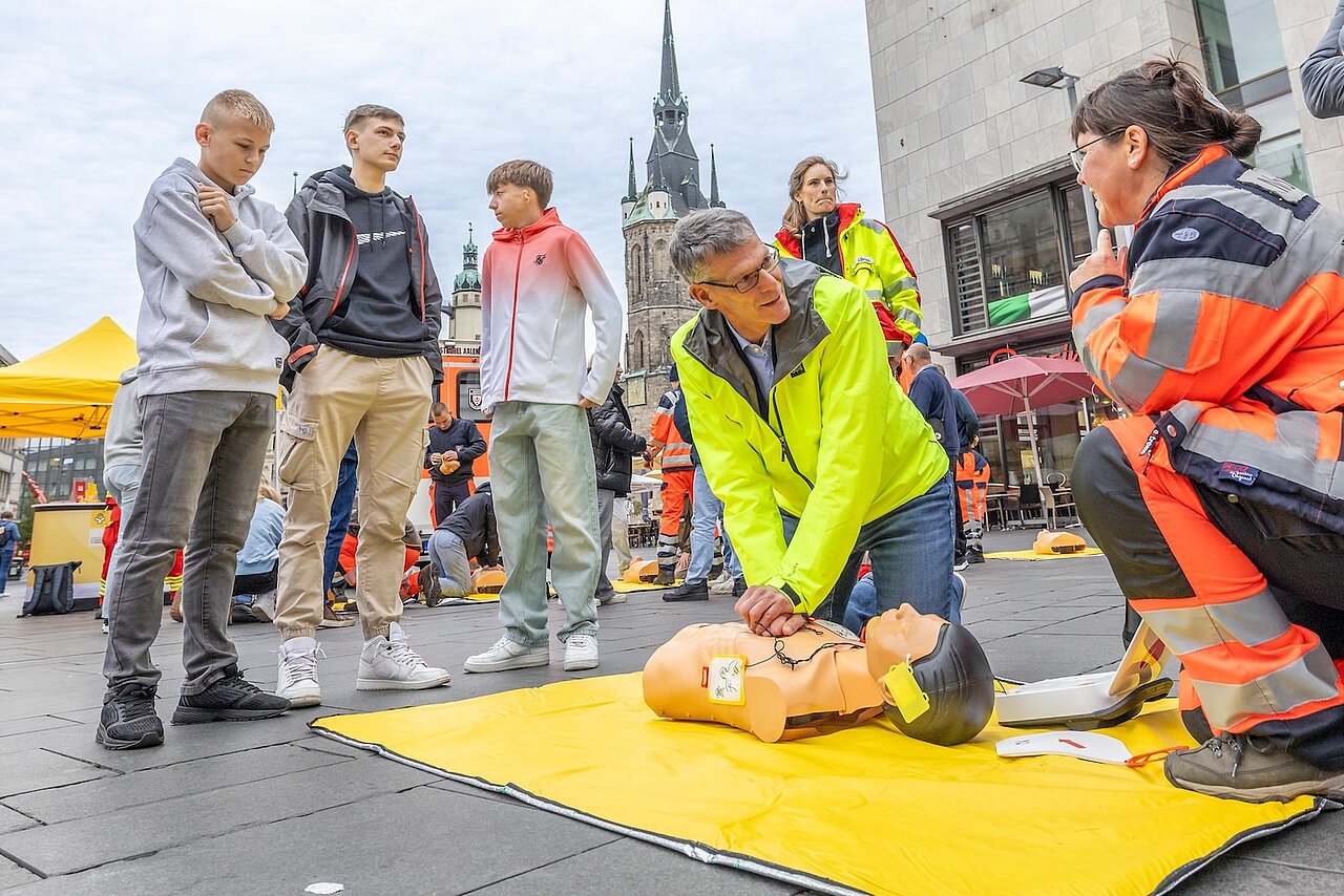 Der Bürgermeister kniet vor einer Oberkörper-Puppe neben einer Sanitäterin.