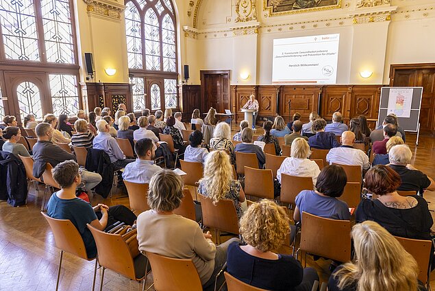 Personen sitzen in mehreren Reihen vor einer Präsentation.