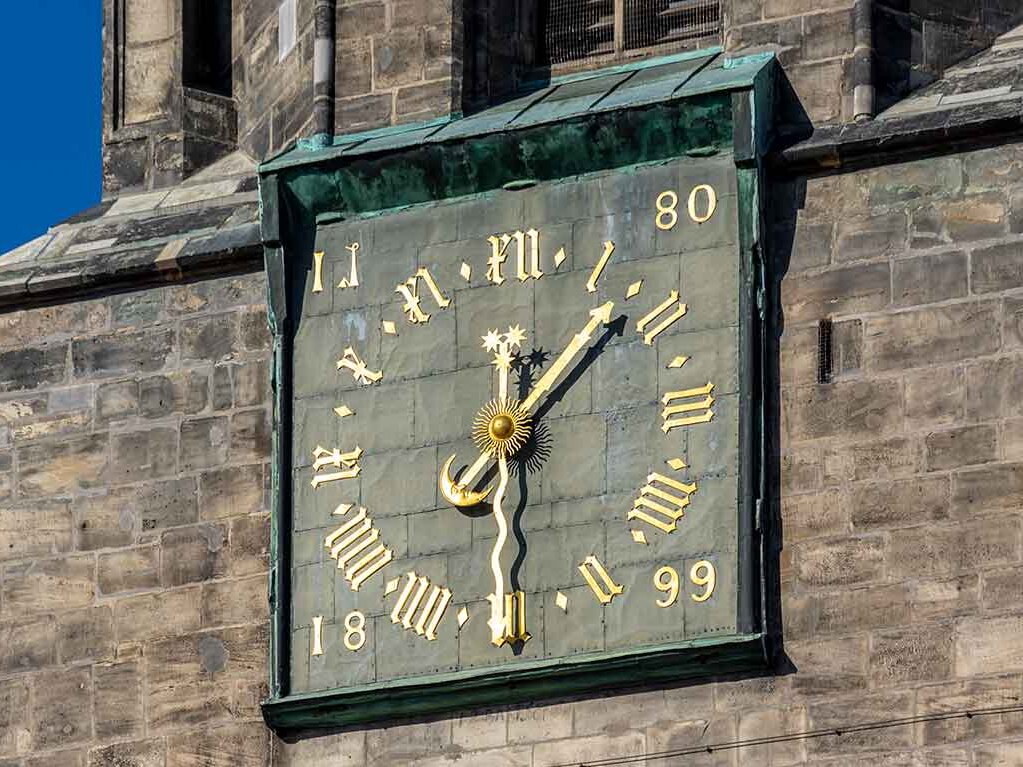 Nahaufnahme des Ziffernblattes der Uhr am Roten Turm. Die römischen Zahlen und die Zeiger sind goldfarben