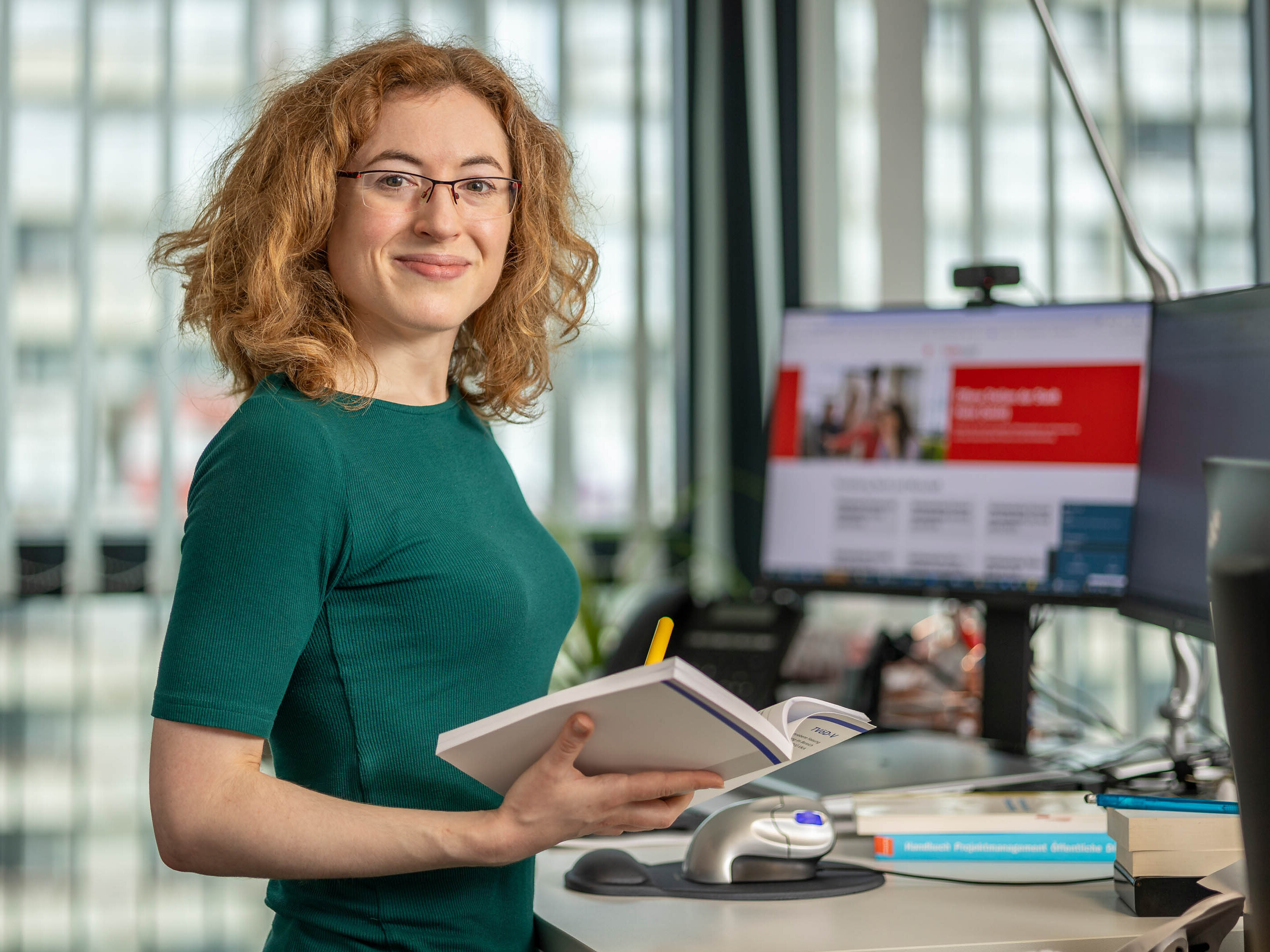 Irene Mathieu am Büroarbeitsplatz, ehemalige duale Studentin der öffentlichen Verwaltung bei der Stadtverwaltung Halle (Saale) ist jetzt Sachbearbeiterin bei der Stadtverwaltung Halle (Saale), abgebildet an Ihrem Büroarbeitsplatz mit einem Buch in der Hand