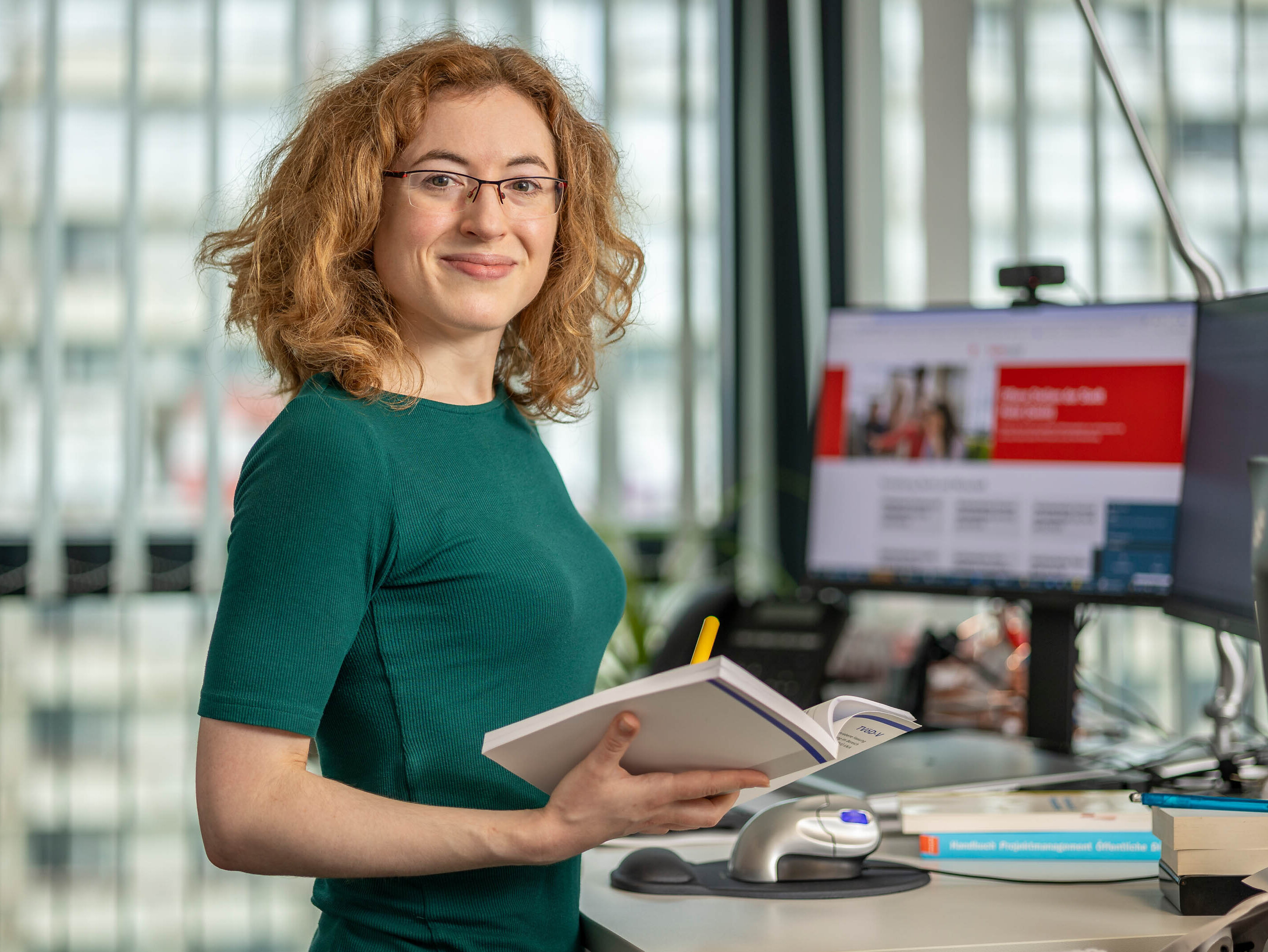 Irene Mathieu am Büroarbeitsplatz, ehemalige duale Studentin der öffentlichen Verwaltung bei der Stadtverwaltung Halle (Saale) ist jetzt Sachbearbeiterin bei der Stadtverwaltung Halle (Saale), abgebildet an Ihrem Büroarbeitsplatz mit einem Buch in der Hand