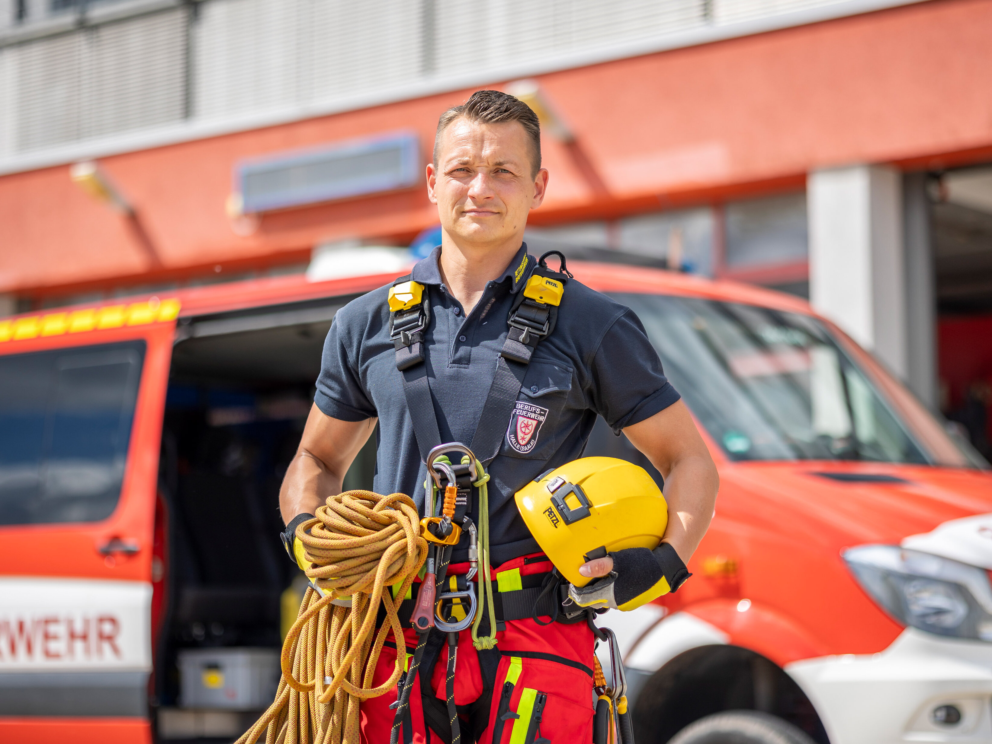 Christian Häußler, Brandmeister bei der Berufsfeuerwehr Halle (Saale), abgebildet vor dem EInsatzfahrzeug und ausgerüstet als Höhenretter