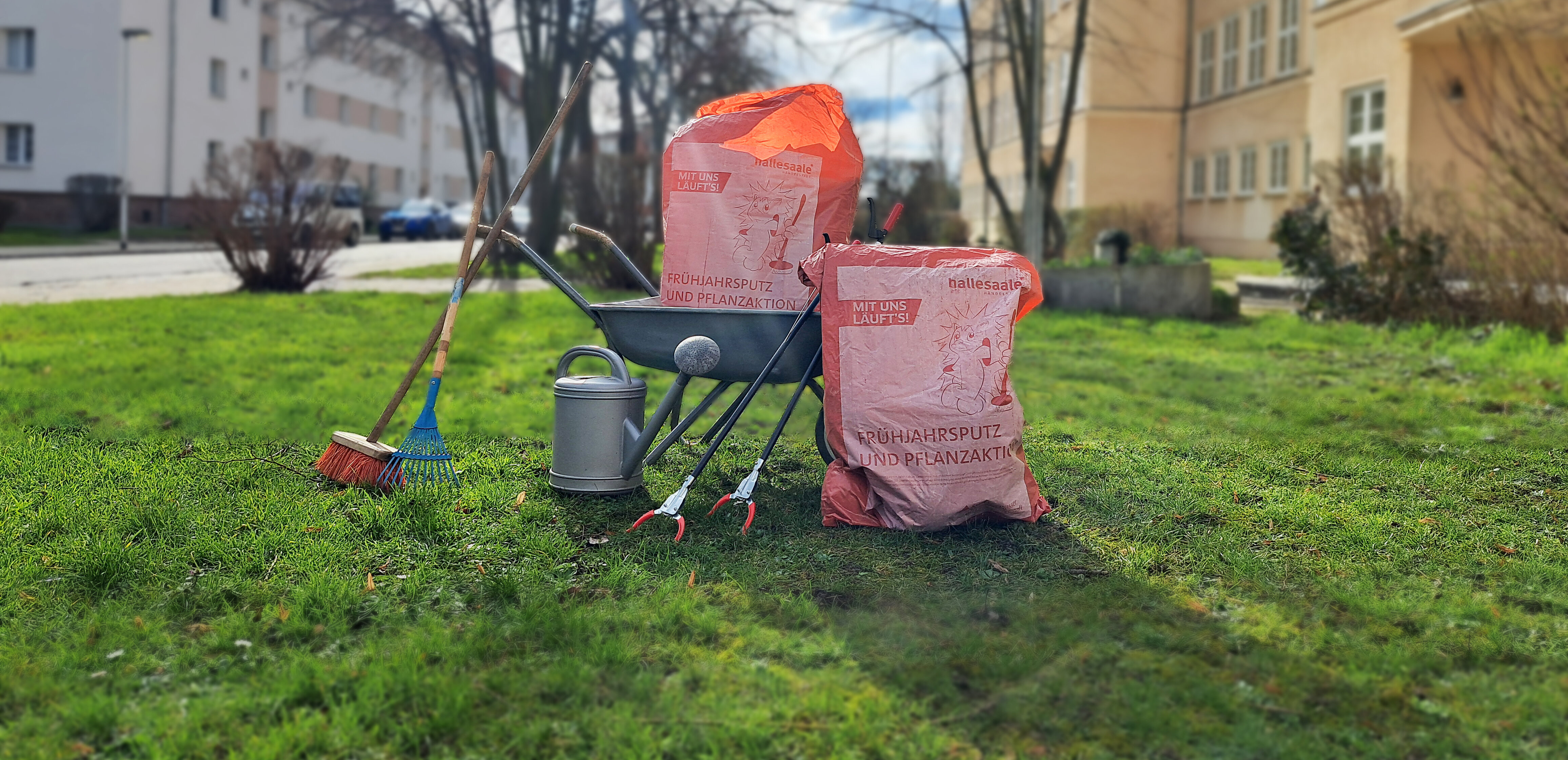 Frühjahrsputzsäcke platziert auf einer Wiese mit Schubkarre, Besen und Greifzangen
