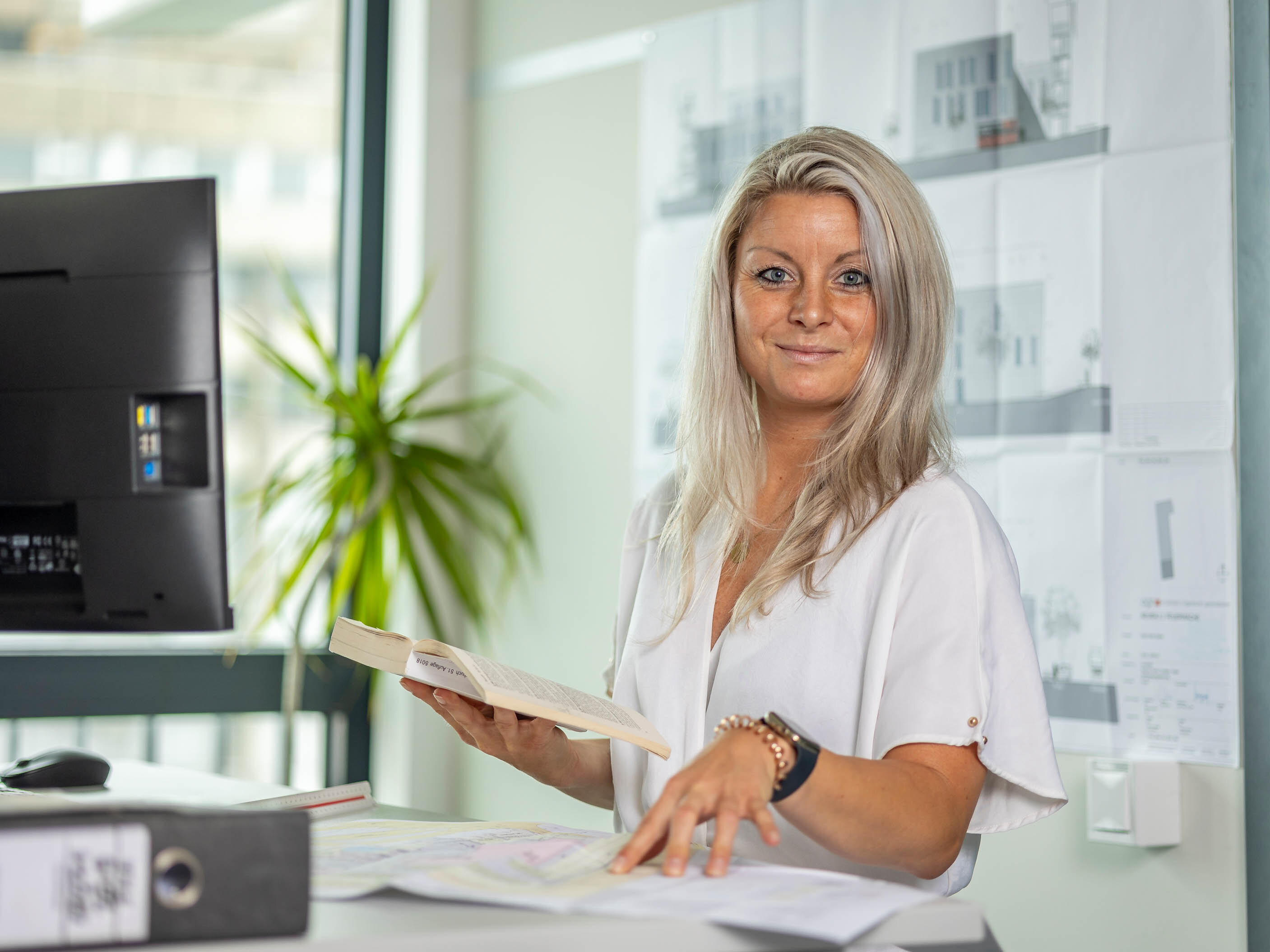 Antje Zimmerling, Architektin ist als Sachbearbeiterin Baugesuchsprüfung in der Stadtverwaltung tätig, Sie ist an ihrem Schreibtisch mit Bauplänen und hat ein Buch in der Hand