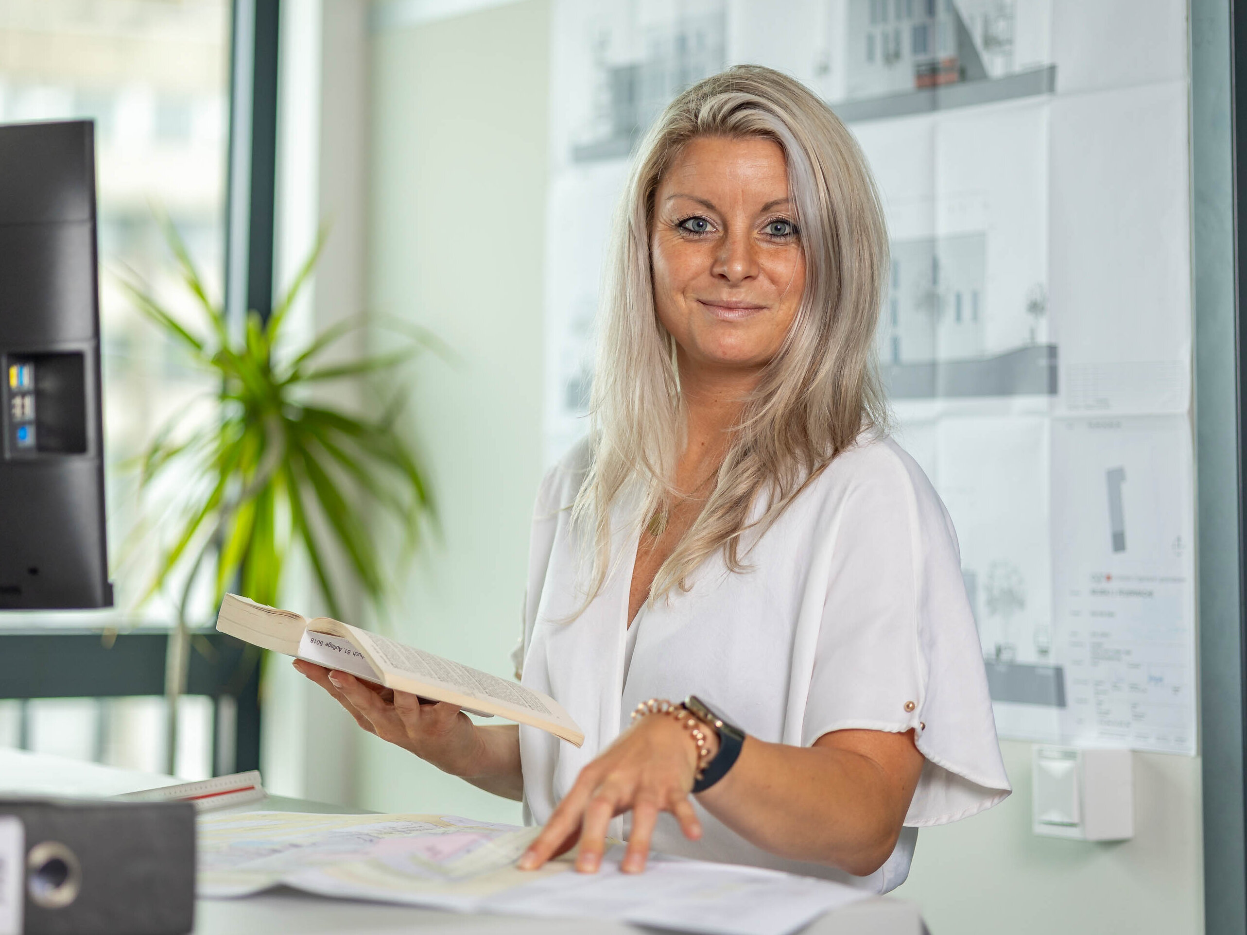 Antje Zimmerling, Architektin ist als Sachbearbeiterin Baugesuchsprüfung in der Stadtverwaltung tätig, Sie ist an ihrem Schreibtisch mit Bauplänen und hat ein Buch in der Hand