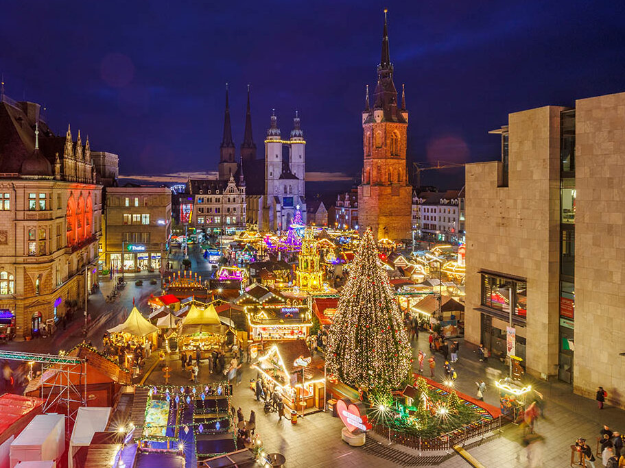 Blick auf den Weihnachtsmarkt auf dem Halleschen Marktplatz am Abend mit beleuchtetem Baum