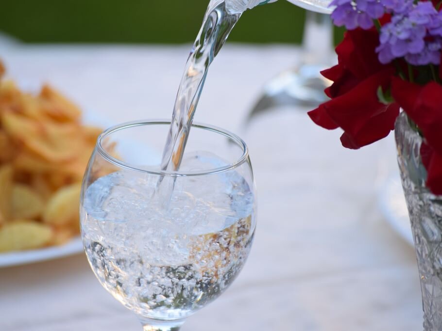 Wasserglas wird mit Mineralwasser gefüllt, im Hintergrund gedeckter Tisch