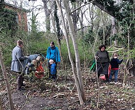 Das Foto zeigt Frauen mit Kindern, die im Gehölz Streumüll aufsammeln.