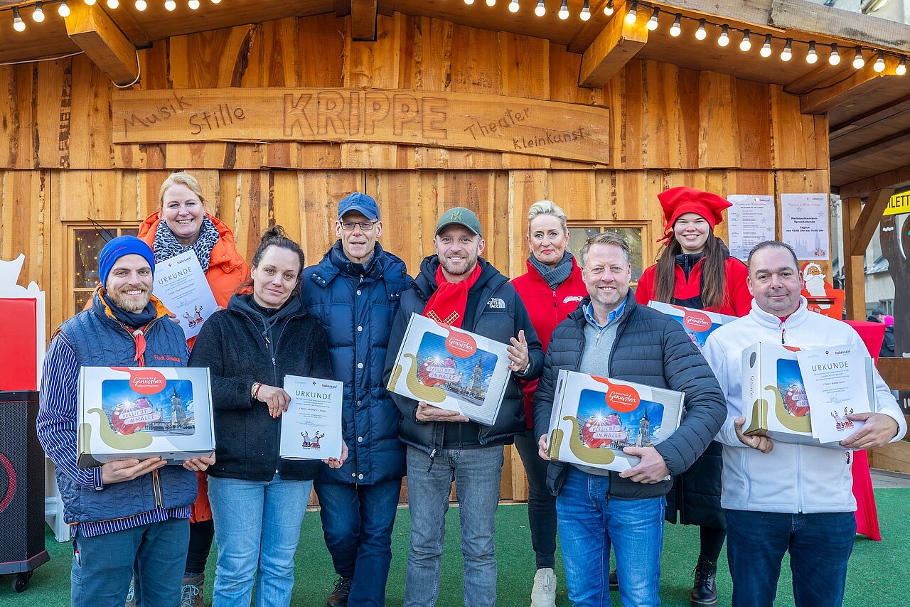 Gruppe von neun Menschen stehen vor eien Hütte mit Urkunden in den Händen.