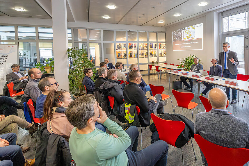 Bürgermeister Egbert Geier steht vor einer Gruppe Zuhörern. Neben ihm im Auditorium sitzen weitere Personen.