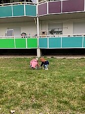 Auf einer Grünfläche hockt ein Kind, das Müll aufliest. Es hält einen Müllsack in der Hand.