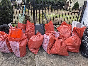 Foto, auf dem ca. 10 befüllte Müllsäcke vor einem Gartentor stehen.