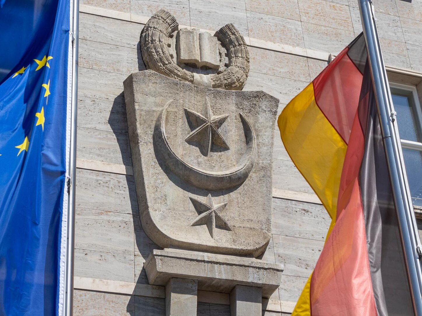 Es ist das Stadtwappen an dem Ratshof mit den davor wehenden Fahnen für Europa, Deutschland und Sachsen-Anhalt zu erkennen.
