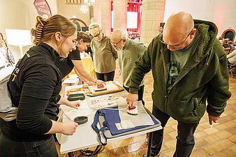 Ehrenamtliche informieren sich bei den Vertreterinnen der Freiwilligen-Agentur Halle-Saalkreis e.V. und nehmen Angebot wahr (Stoffbeutel werden bedruckt).