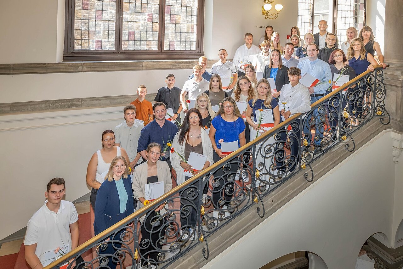 Die Personen stehen mit Urkunde und Blumen in der Hand auf der Treppe.