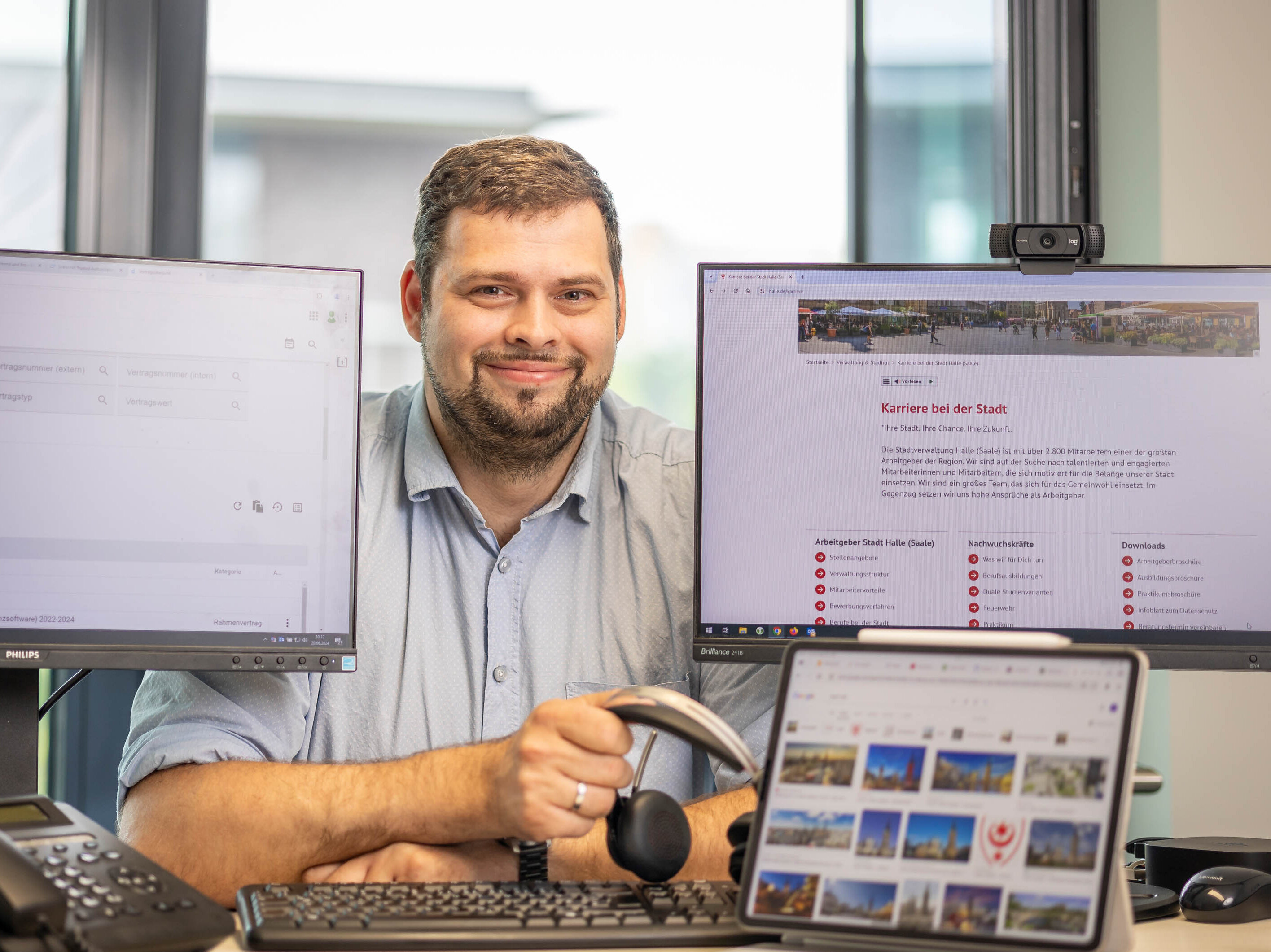 Sven Götze, Vertrags-/Lizenz- und Berechtigungsmanager in der Abteilung IT und Digitale Verwaltung der Stadt Halle zwischen mehreren Bildschirmen und einem Headset in der Hand