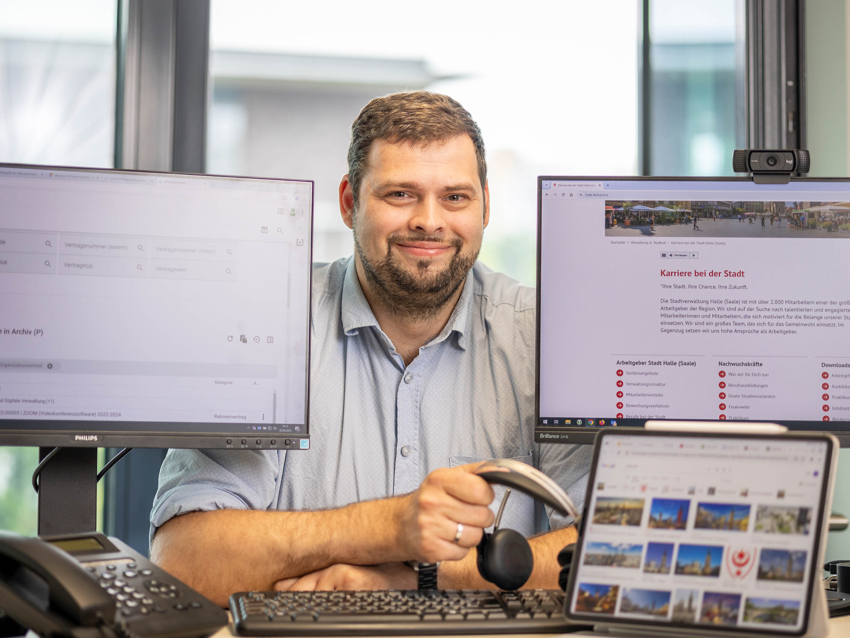 Sven Götze, Vertrags-/Lizenz- und Berechtigungsmanager in der Abteilung IT und Digitale Verwaltung der Stadt Halle zwischen mehreren Bildschirmen und einem Headset in der Hand