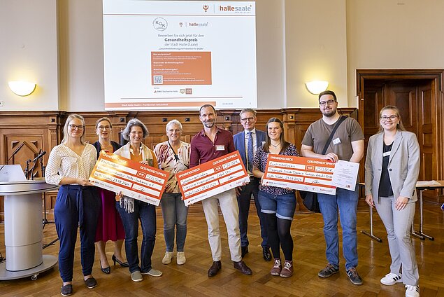 Die Gruppe hält drei Checks mit Preisgeld in der Hand.
