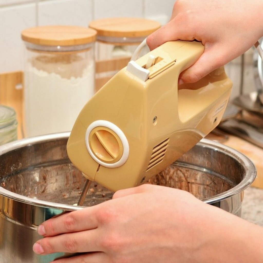 Mit einem beigefarbenen Handmixer wird ein Teig in einer Schüssel gerührt. 