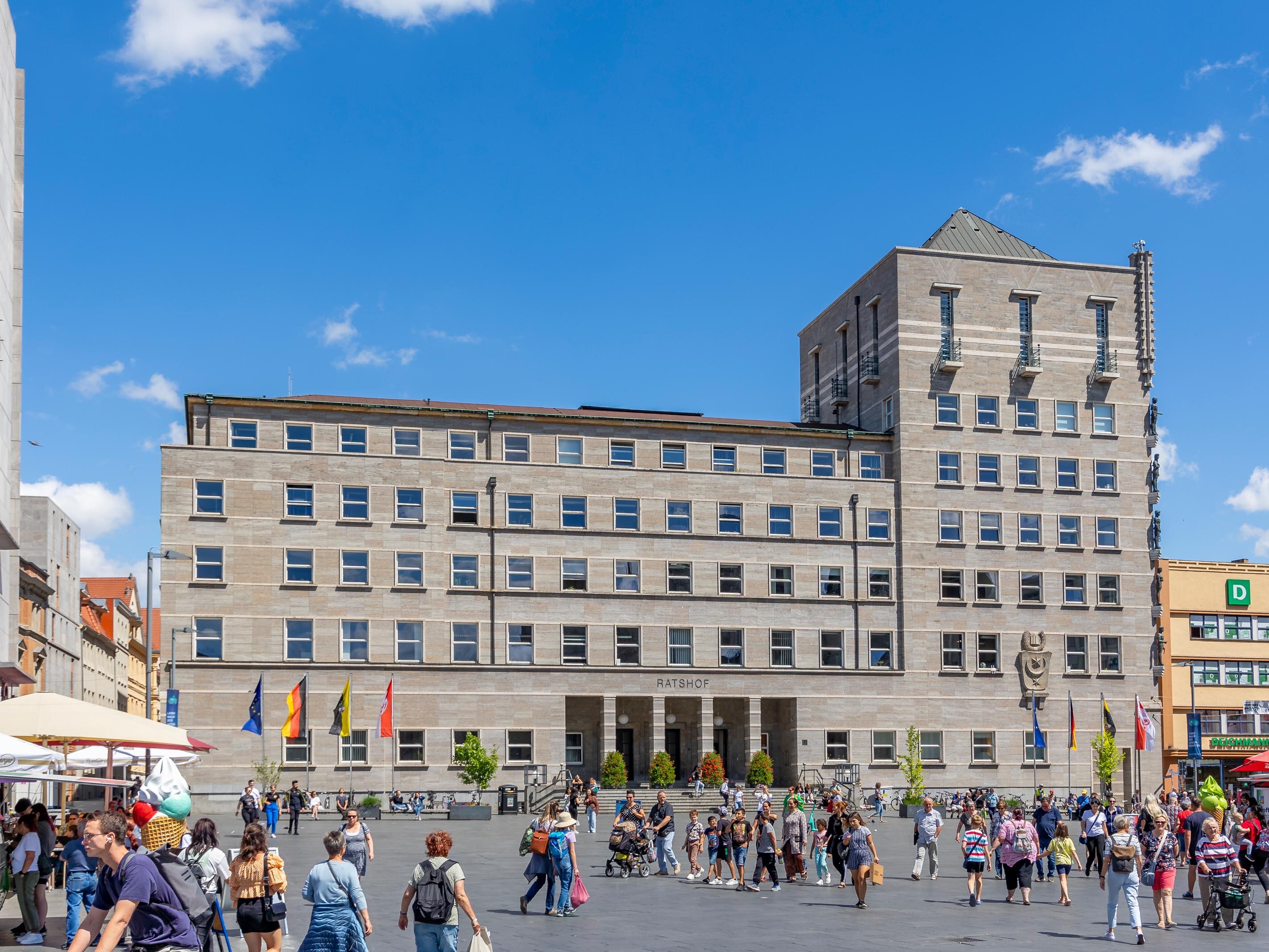 Das Bild zeigt den hallischen Marktplatz mit dem Ratshof als Bildzentrum. Auf dem Marktplatz herrscht ein alltägliches Treiben mit vielen Menschen.