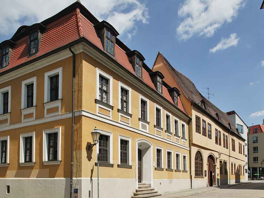 Blick auf das Händelhaus, dem Geburtshaus Georg Friedrich Händels, in einer Straße inmitten der Altstadt. Das Haus hat gelbe Mauern und ein rotes Dach und beherbergt heute ein Museum über Händel