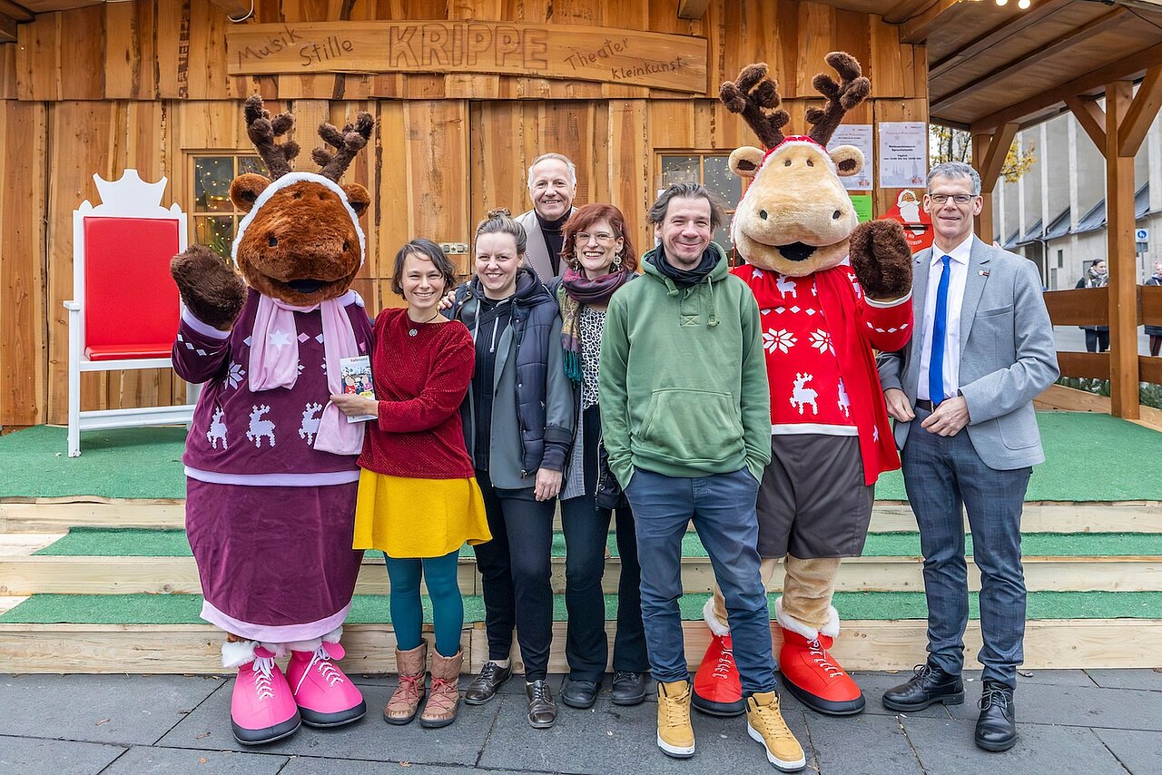 Die Personen stehen nebeneinander vor einer Hütte mit Maskottchen.