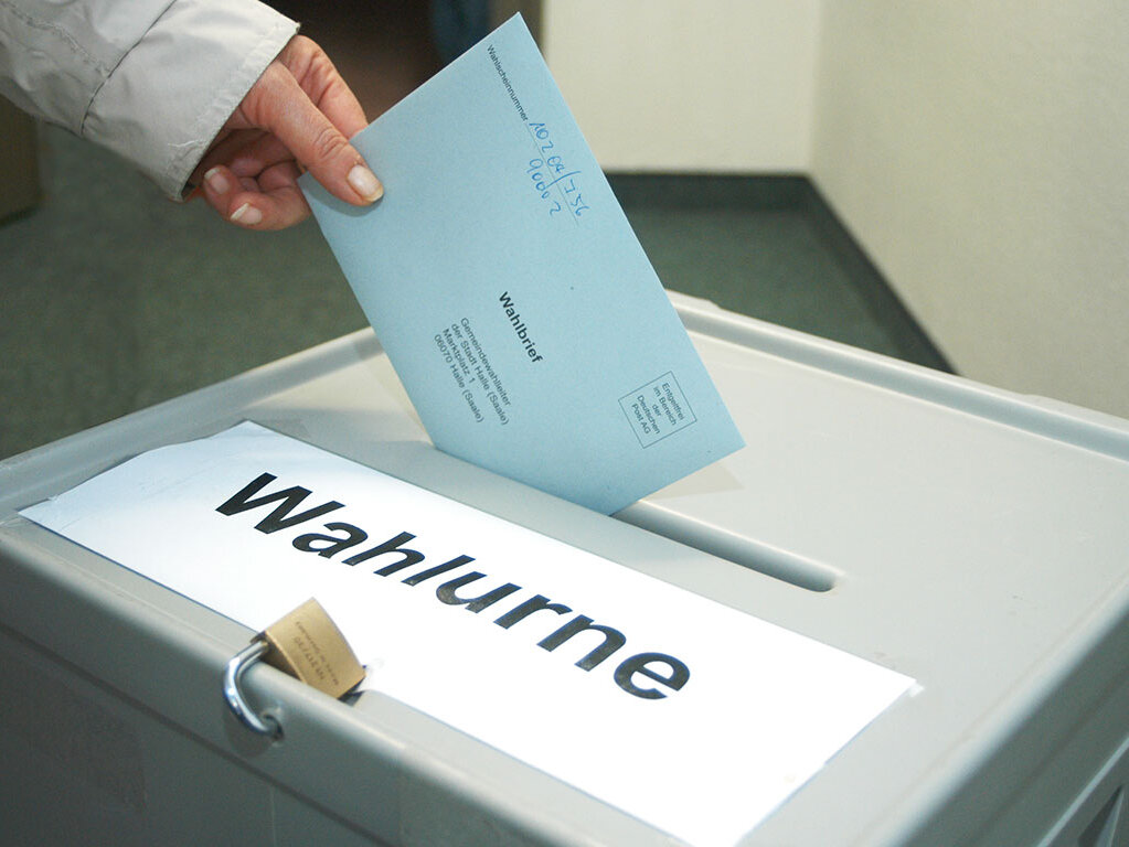 Eine Hand wirft einen Stimmzettel in eine Wahlurne