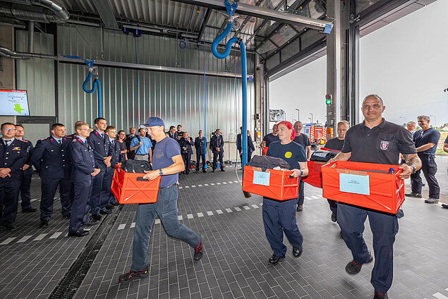 Feuerwehrleute laufen mit roten Kisten in der Hand in die neue Wache.