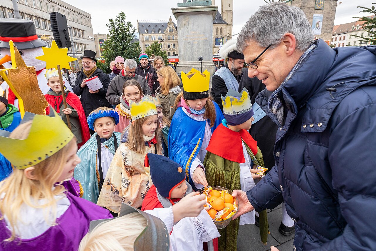 Egbert Geier steht umringt von Kindern mit einer Schale voller Orangen in der Hand.