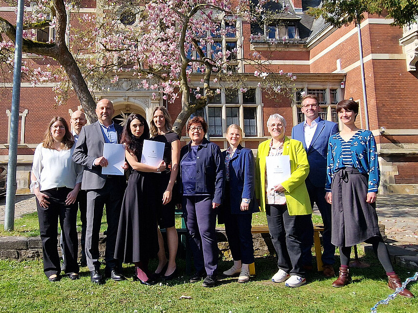 Gruppe von zehn Menschen vor einem Gebäude. Sachsen-Anhalts Sozialministerin Petra Grimm-Benne (Mitte) hat in Dessau-Roßlau die Fördermittelbescheide für das Modellvorhaben MUvIS auch an Halles Beigeordnete für Bildung und Soziales, Katharina Brederlow (3.v.r.), überreicht.