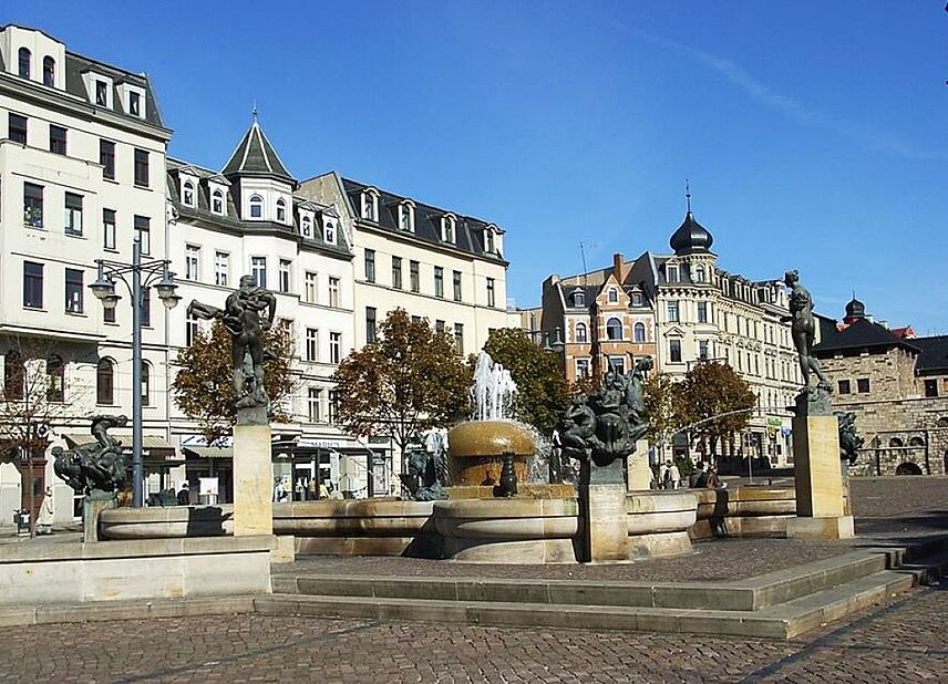 Springbrunnen mit Figuren aus der halleschen Stadtgeschichte, im Hintergrund mehrgeschossige sanierte Wohn- und Geschäftshäuser