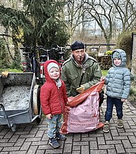 2 Kinder mit einem Erwachsenen, der einen Müllsack in der Hand hält.