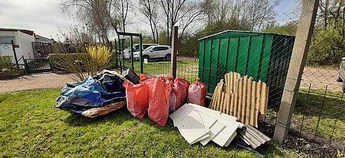 Es stehen mehrere befüllte Müllsäcke und Sperrmüll geordnet vor einem Zaun.