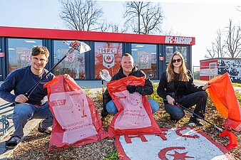Foto zeigt 3 Personen mit Müllsäcken und Greifzangen in der Hand. Im Hintergrund ist der HFC-Fanshop zu sehen.