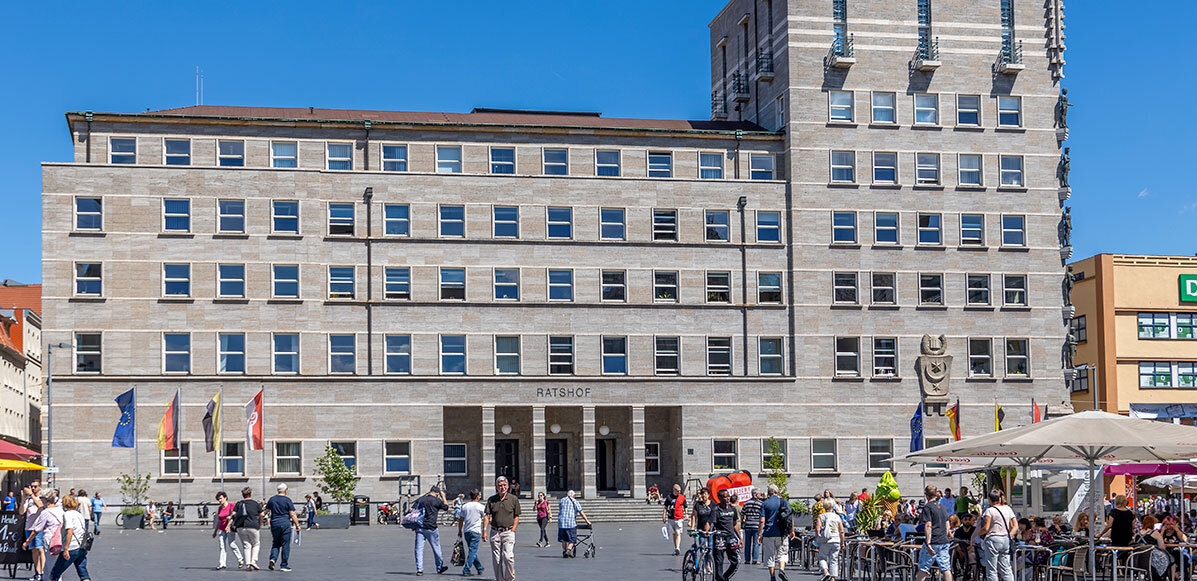 Blick auf das Ratshofsgebäude vom Marktplatz aus, davor laufen Menschen oder stehen an Marktständen