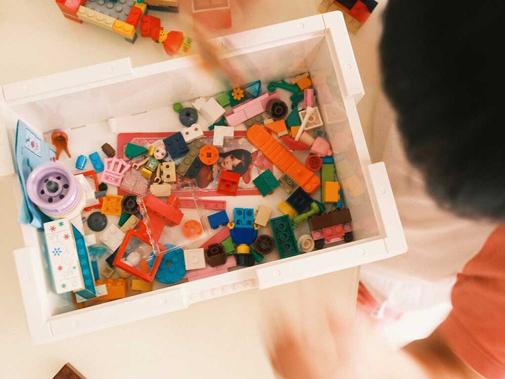 Kind schaut in eine weiße Kiste mit bunte Bausteinen und Kinderspielzeug