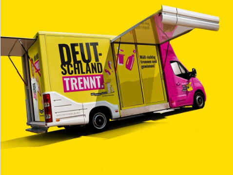 ein gelber Transporter mit Aktionsflächen und Trennbär, ein weißer menschenhöher Plüschbär mit roter Hose