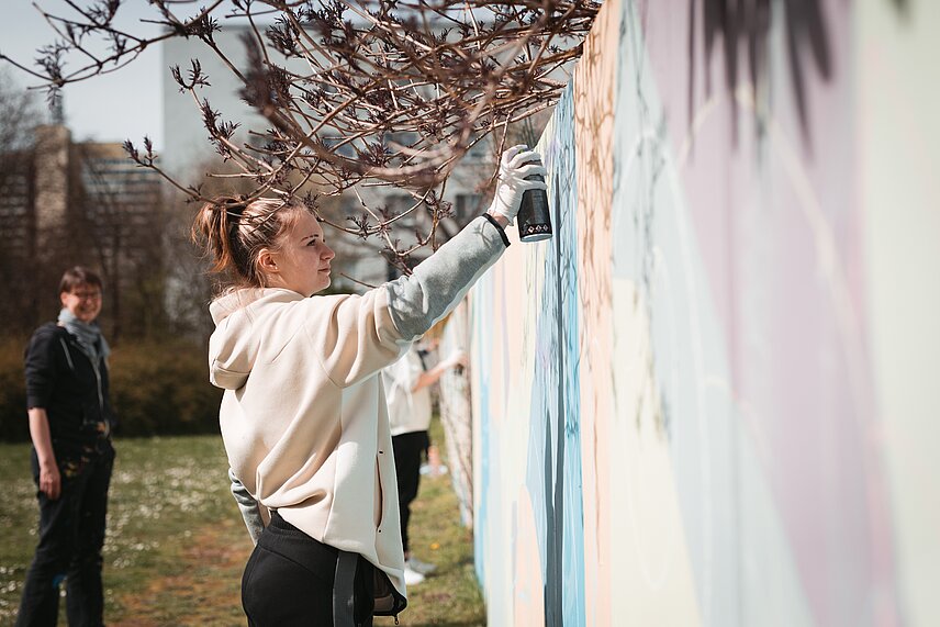 Junge Frau sprüht in einem Kunstobjekt ein Wandbild der GWG Halle-Neustadt  
