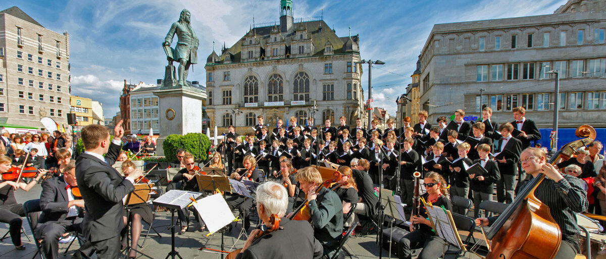 Orchester mit Dirigent und Chor spielen neben Händel-Denkmal auf dem Marktplatz