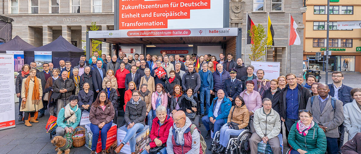 Viel Frauen und Münner - Gründungsmitglieder des Netzwerkes für das Zukunftszentrum in Halle auf dem Marktplatz vor einer Bühne vor dem Ratshof mit der Aufschrift Halle bewirbt sich um das Zukunftszentrum für Deutsche Einheit und Europäische Transformation