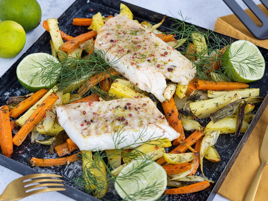 Zwei Fischfilets auf Blech mit Ofengemüse (Karotten und Kartoffeln), dazu Limetten und Dill.