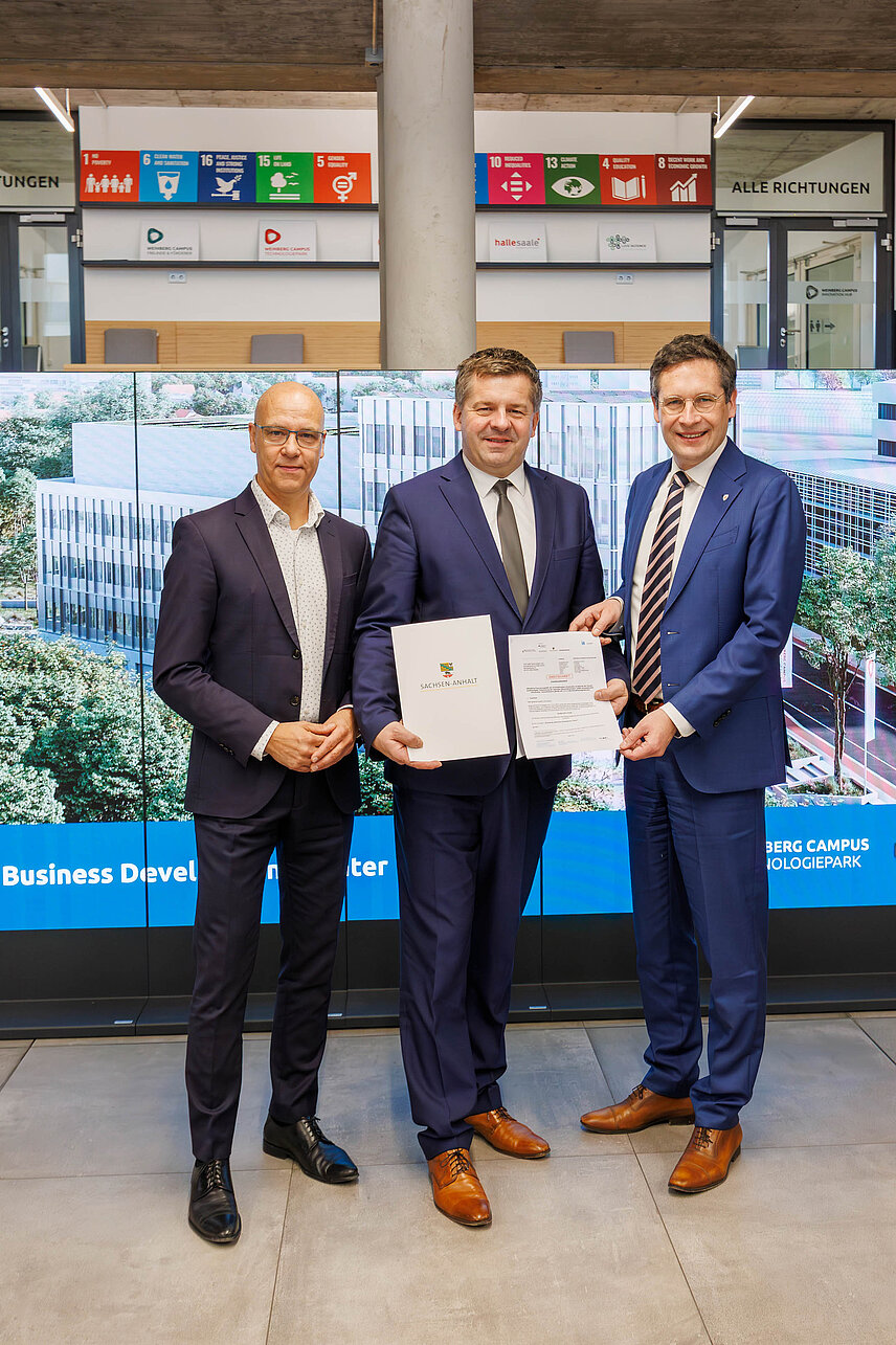 Drei Männer halten den die Urkunde des Förderbescheids