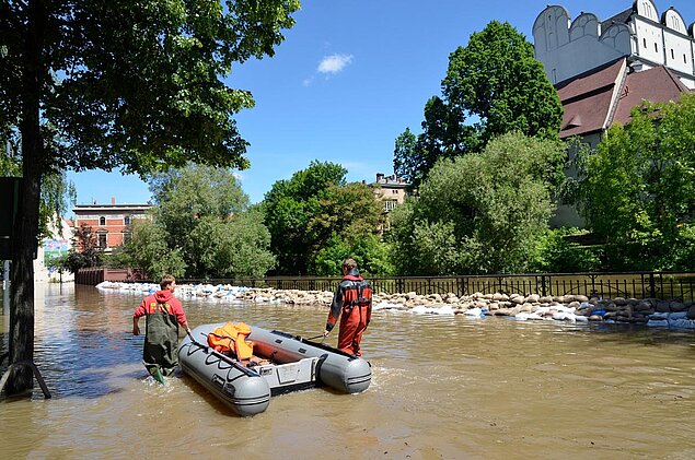 Hilfskräfte waten mit Schlauchboot über überspülten Brücke am Robert-Franz-Ring