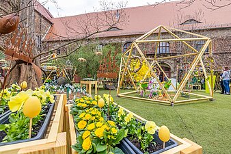 geodätische Figut aus Holzbalken gebaut, im Vordergrund Hochbeete aus hellem Holz mit gelben Blumen bestückt